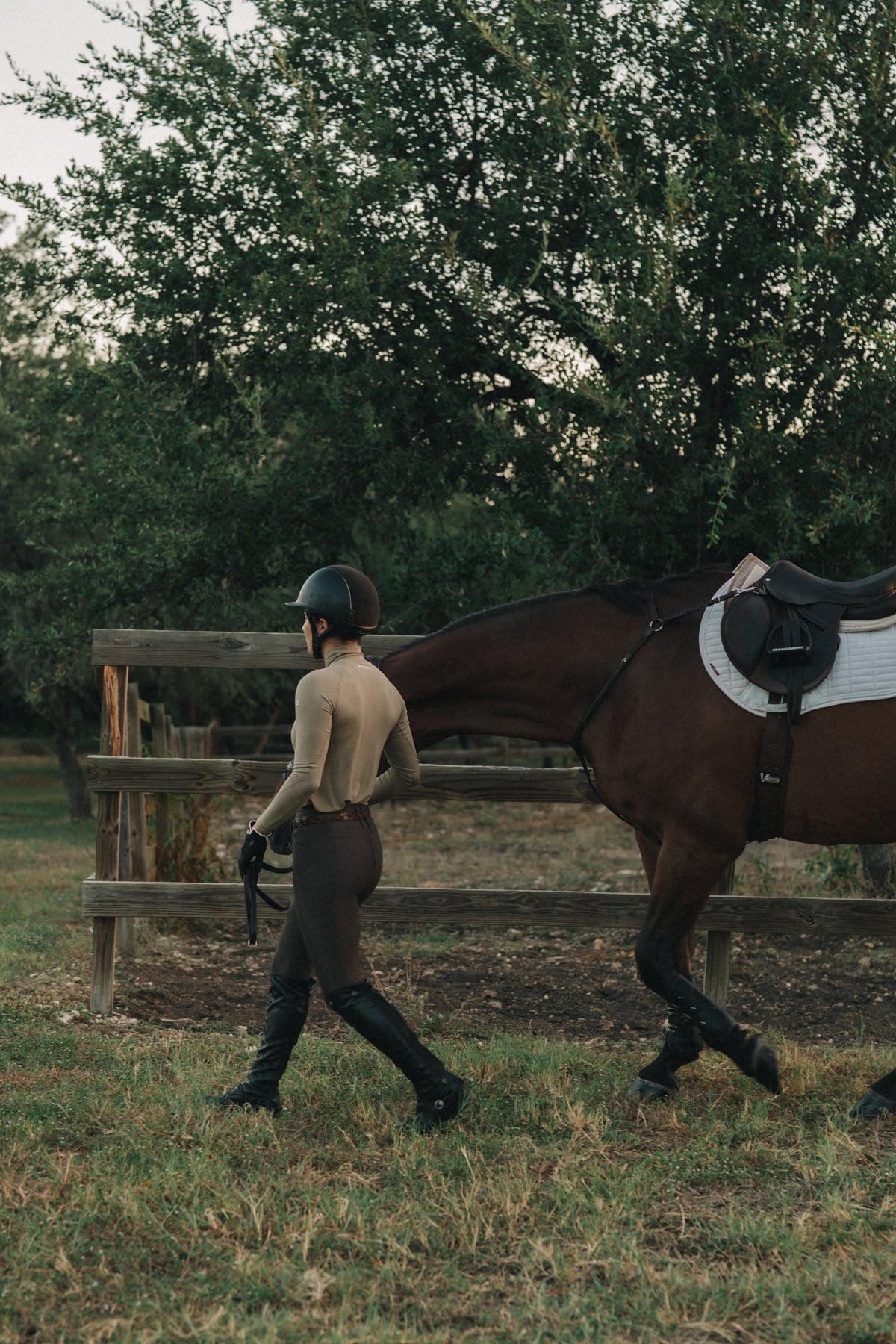 Rider in the khaki Mia Mock Neck leading a horse past the fence