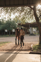 Rider in the khaki Mia Mock Neck walking a horse out of the stables
