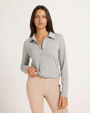 Woman wearing a light gray button-up shirt and beige pants on a white background