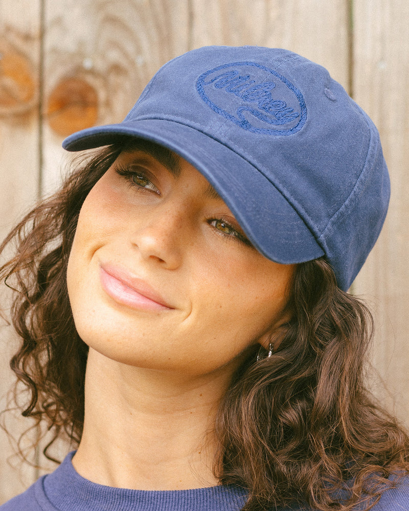 Woman wearing a navy cap with a logo against a wooden background