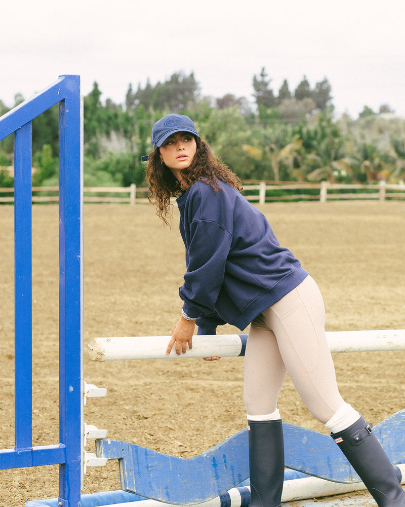 Person in equestrian attire standing next to a blue jump in an outdoor setting