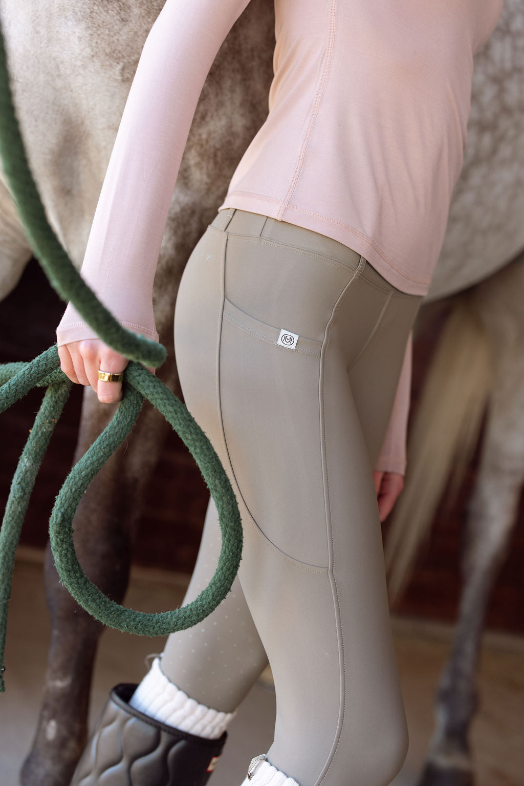Person wearing beige riding pants holding a green rope with a horse in the background